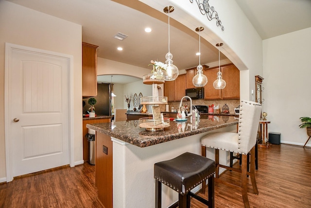 kitchen featuring a kitchen breakfast bar, tasteful backsplash, visible vents, brown cabinetry, and black appliances
