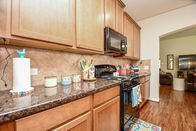 kitchen with dark stone countertops, wood finished floors, black appliances, decorative backsplash, and open floor plan