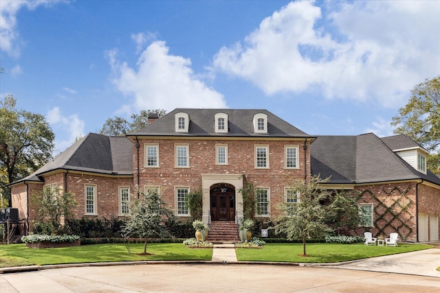 georgian-style home featuring brick siding, a front lawn, a chimney, and cooling unit