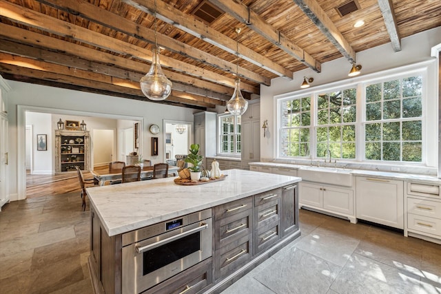 kitchen featuring wooden ceiling, a sink, white cabinets, beamed ceiling, and light stone counters
