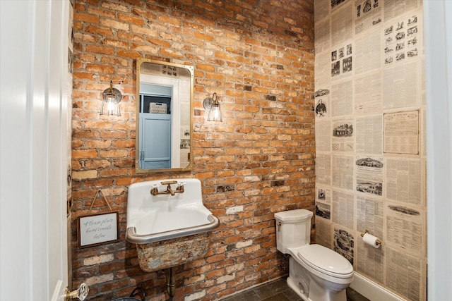 bathroom with brick wall, toilet, and a sink