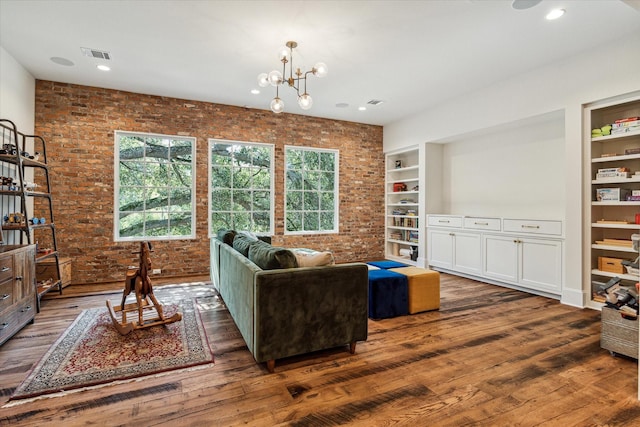 living area featuring brick wall, wood finished floors, built in shelves, and a chandelier
