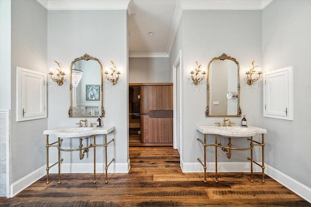 bathroom with wood finished floors, ornamental molding, baseboards, and two sinks