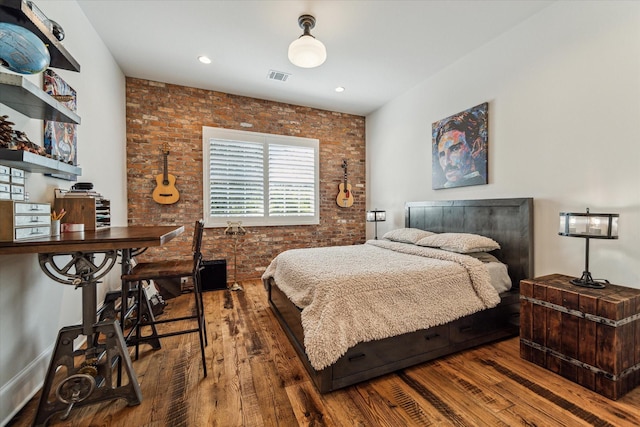 bedroom with wood finished floors and brick wall