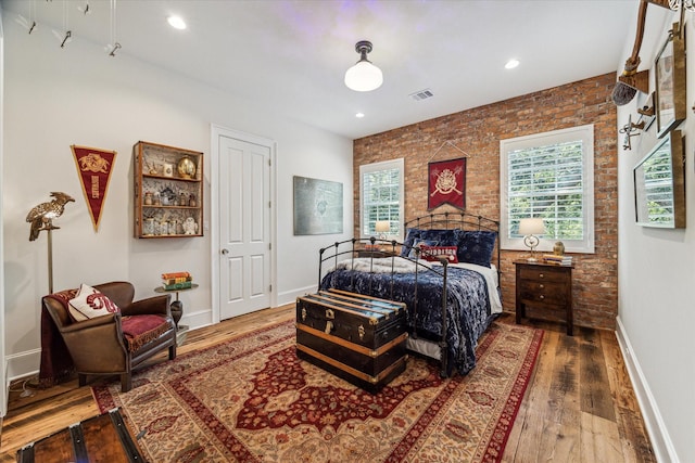 bedroom featuring wood finished floors, baseboards, brick wall, and recessed lighting