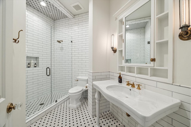 full bath featuring a stall shower, toilet, tile walls, a sink, and wainscoting