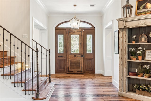 foyer with wood finished floors, stairway, a chandelier, ornamental molding, and baseboards