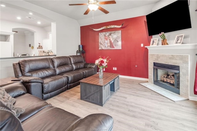 living area featuring a ceiling fan, light wood-type flooring, arched walkways, a fireplace, and recessed lighting