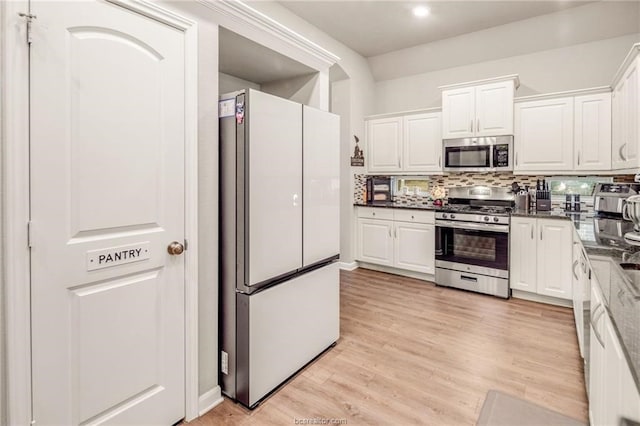 kitchen with light wood finished floors, appliances with stainless steel finishes, tasteful backsplash, and white cabinetry