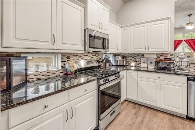 kitchen featuring white cabinets, dark stone countertops, light wood-type flooring, decorative backsplash, and appliances with stainless steel finishes