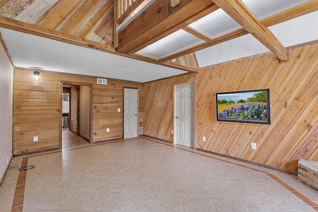 spare room with wood walls, beamed ceiling, tile patterned floors, and visible vents