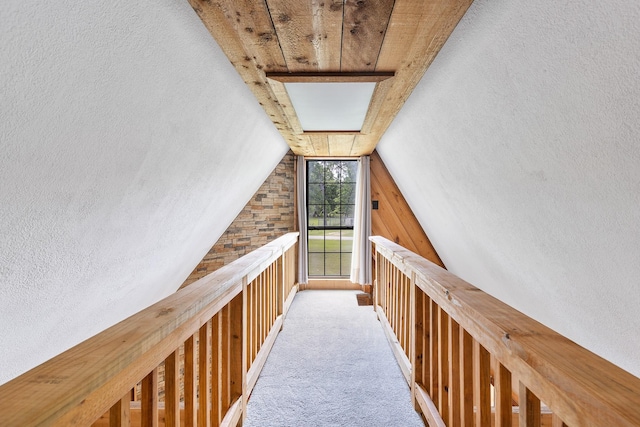 corridor with lofted ceiling, a textured wall, and carpet
