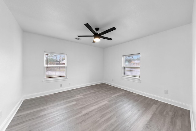 spare room with wood finished floors, visible vents, a ceiling fan, and baseboards