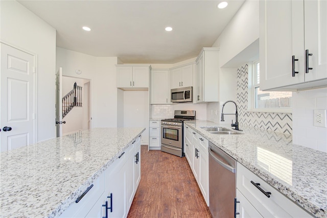 kitchen with a sink, stainless steel appliances, white cabinetry, dark wood-style flooring, and light stone countertops