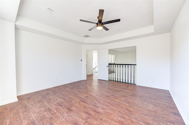 empty room featuring a ceiling fan, wood finished floors, visible vents, and a raised ceiling