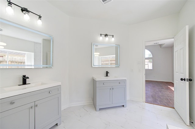 full bathroom with two vanities, marble finish floor, baseboards, and a sink