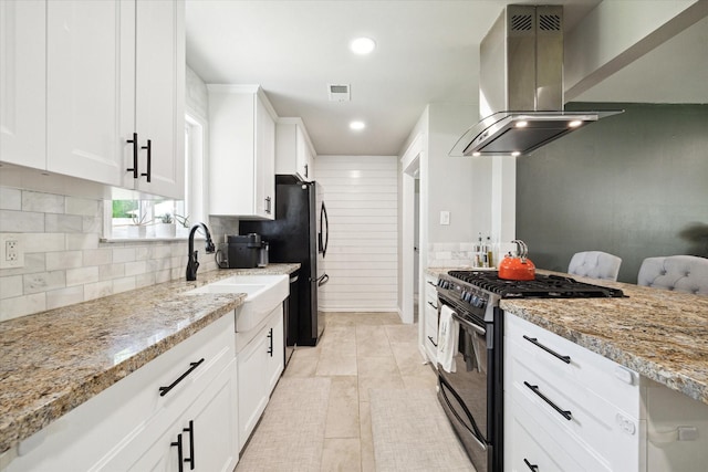 kitchen featuring ventilation hood, light stone counters, backsplash, visible vents, and black gas range
