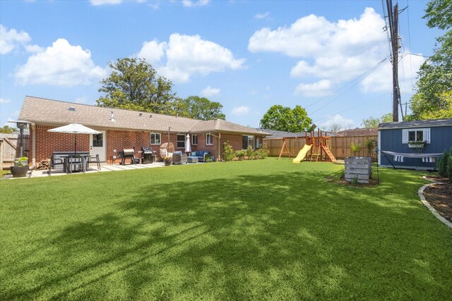 view of yard with a patio area, a shed, a playground, a fenced backyard, and an outbuilding