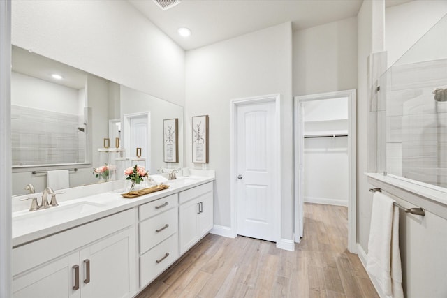 full bathroom with wood finished floors, a sink, double vanity, and a tile shower