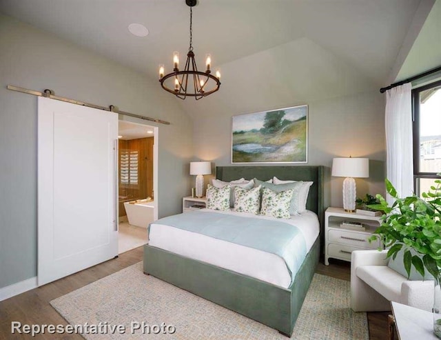 bedroom with a barn door, vaulted ceiling, wood finished floors, ensuite bathroom, and an inviting chandelier