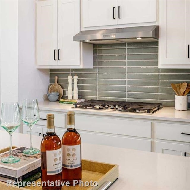kitchen with stainless steel gas stovetop, ventilation hood, light countertops, tasteful backsplash, and white cabinetry
