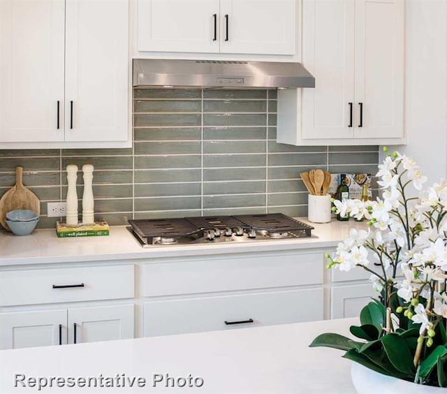 kitchen featuring decorative backsplash, light countertops, under cabinet range hood, and white cabinetry