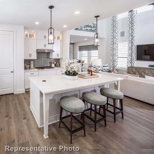 kitchen featuring gas cooktop, glass insert cabinets, a kitchen bar, white cabinets, and dark wood-type flooring