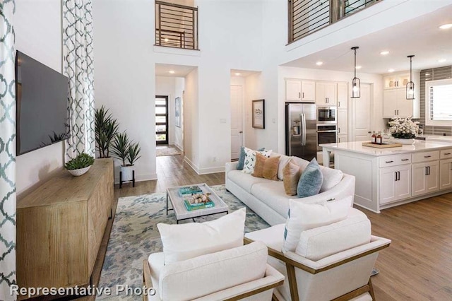 living area with recessed lighting, light wood-type flooring, a high ceiling, and baseboards
