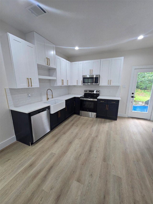 kitchen featuring a sink, light countertops, stainless steel appliances, light wood-style flooring, and white cabinetry