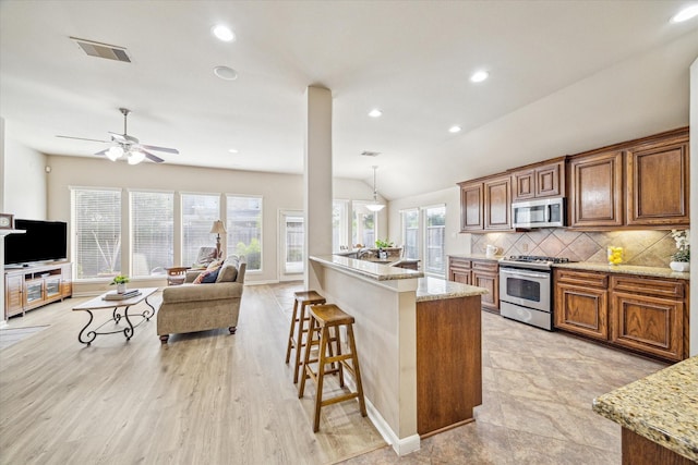 6315 Teal Mist Ln, Fulshear, TX 77441 - kitchen with brown cabinetry, a breakfast bar area, visible vents, light stone counters, and stainless steel appliances