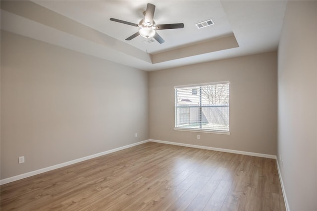 unfurnished room with a tray ceiling, visible vents, light wood-type flooring, baseboards, and ceiling fan