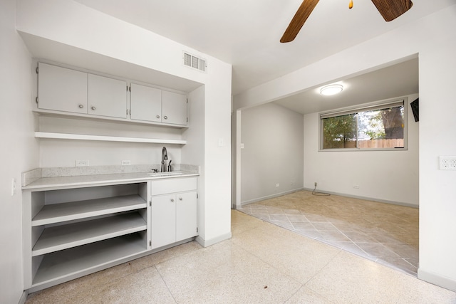 bar featuring a ceiling fan, a sink, baseboards, light speckled floor, and visible vents