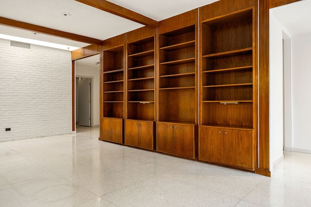 3622 N Braeswood Blvd, Houston, TX 77025 - spare room featuring dark aggregate flooring, brick wall, beam ceiling, built in shelves, and baseboards
