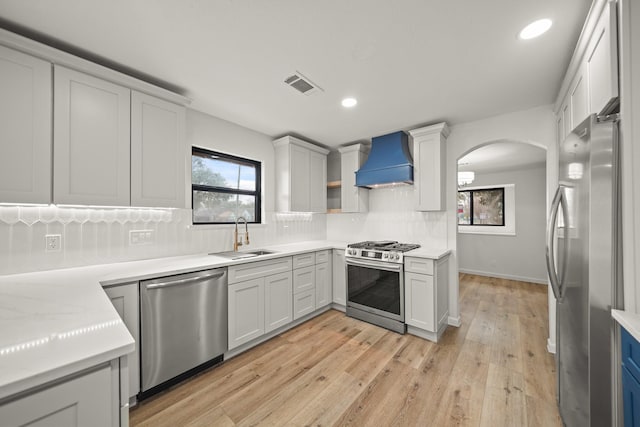 kitchen featuring stainless steel appliances, custom exhaust hood, a sink, arched walkways, and decorative backsplash