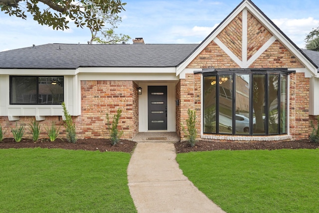 view of front of property featuring a chimney, a front lawn, roof with shingles, and brick siding