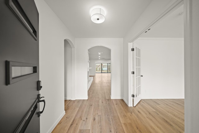 corridor featuring arched walkways, light wood finished floors, and baseboards