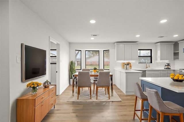 kitchen with light wood-style floors, light countertops, a breakfast bar, a sink, and decorative backsplash