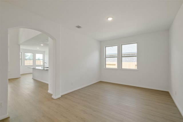 unfurnished room featuring arched walkways, light wood-style floors, visible vents, and recessed lighting