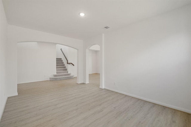 unfurnished living room with light wood-style flooring, baseboards, arched walkways, and stairs