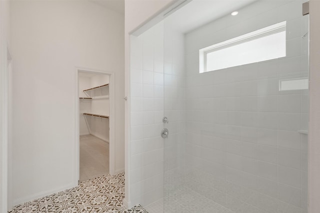 bathroom featuring a spacious closet, a tile shower, baseboards, and tile patterned flooring