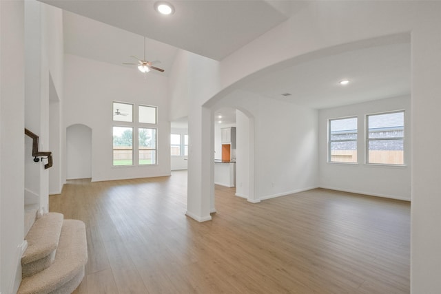 unfurnished living room featuring arched walkways, stairway, light wood finished floors, and ceiling fan