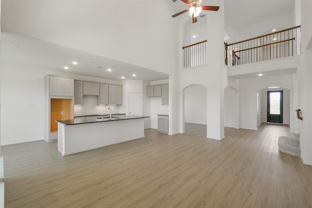 unfurnished living room with stairway, a sink, a towering ceiling, and light wood-style floors