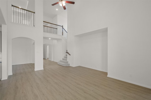 unfurnished living room featuring a ceiling fan, wood finished floors, arched walkways, and stairs