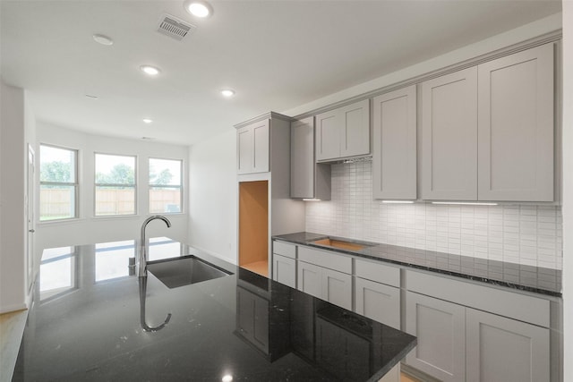 kitchen with a sink, dark stone countertops, visible vents, recessed lighting, and decorative backsplash