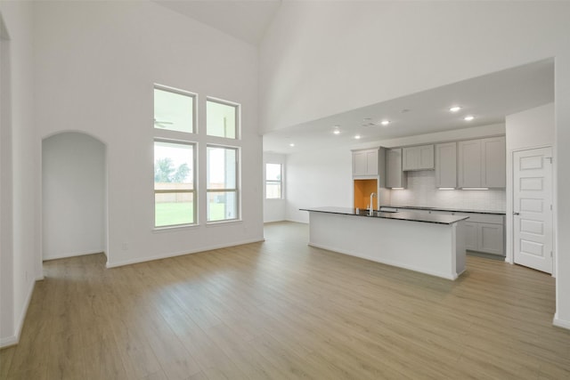 kitchen with light wood finished floors, arched walkways, a sink, a towering ceiling, and backsplash