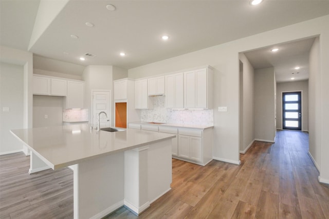 kitchen with white cabinetry, a large island, decorative backsplash, and a sink