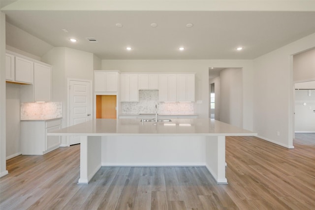 kitchen featuring white cabinets, decorative backsplash, a sink, and a spacious island