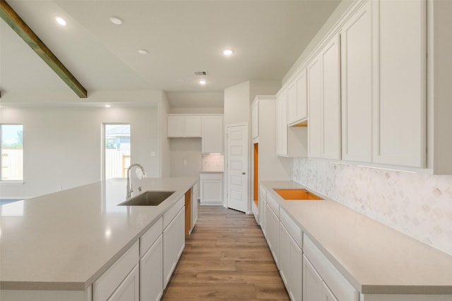 kitchen with an island with sink, a sink, light wood-style floors, decorative backsplash, and white cabinetry