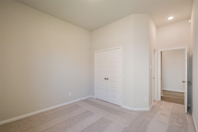unfurnished bedroom featuring light carpet, baseboards, recessed lighting, and a closet