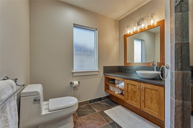 full bathroom featuring baseboards, stone tile flooring, vanity, and toilet